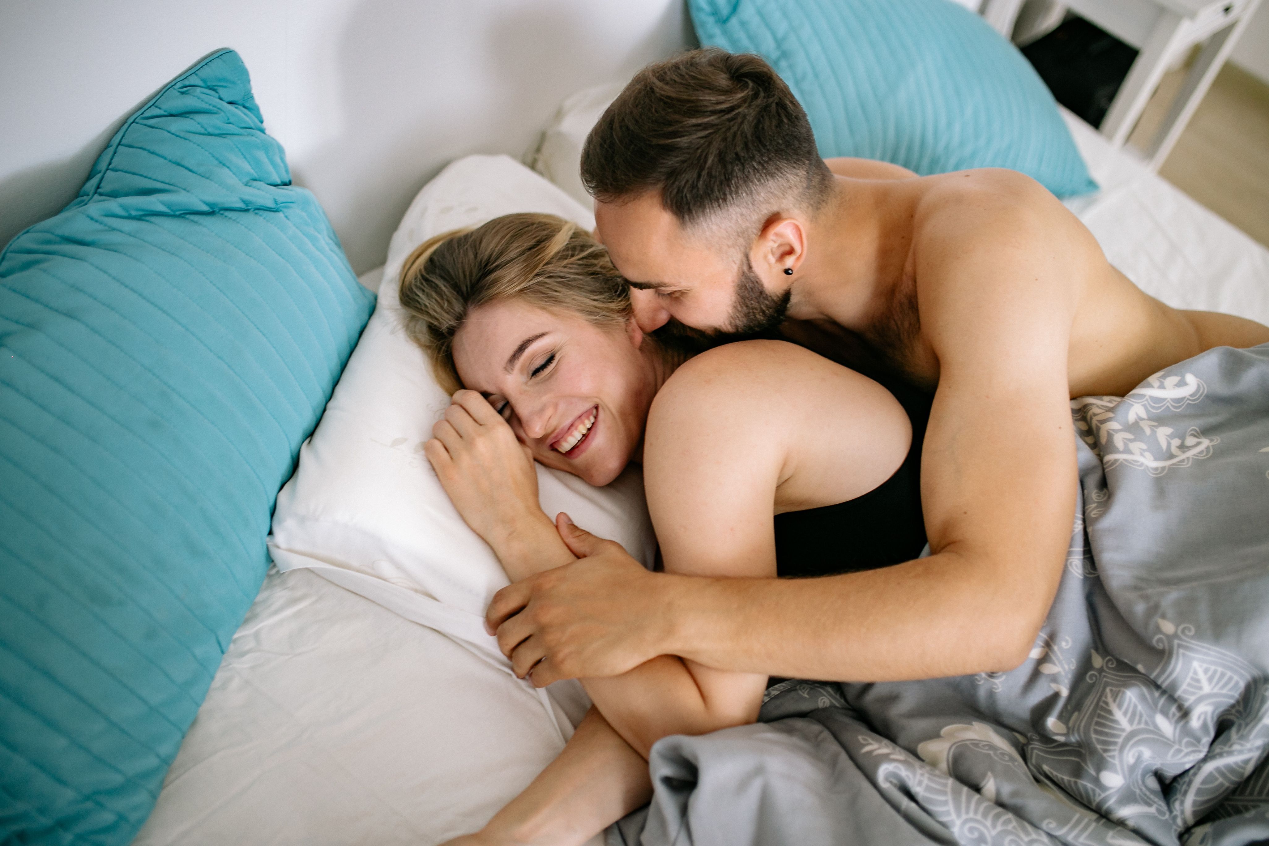 straight couple hugging each other while laying on bed with white and blue pillows