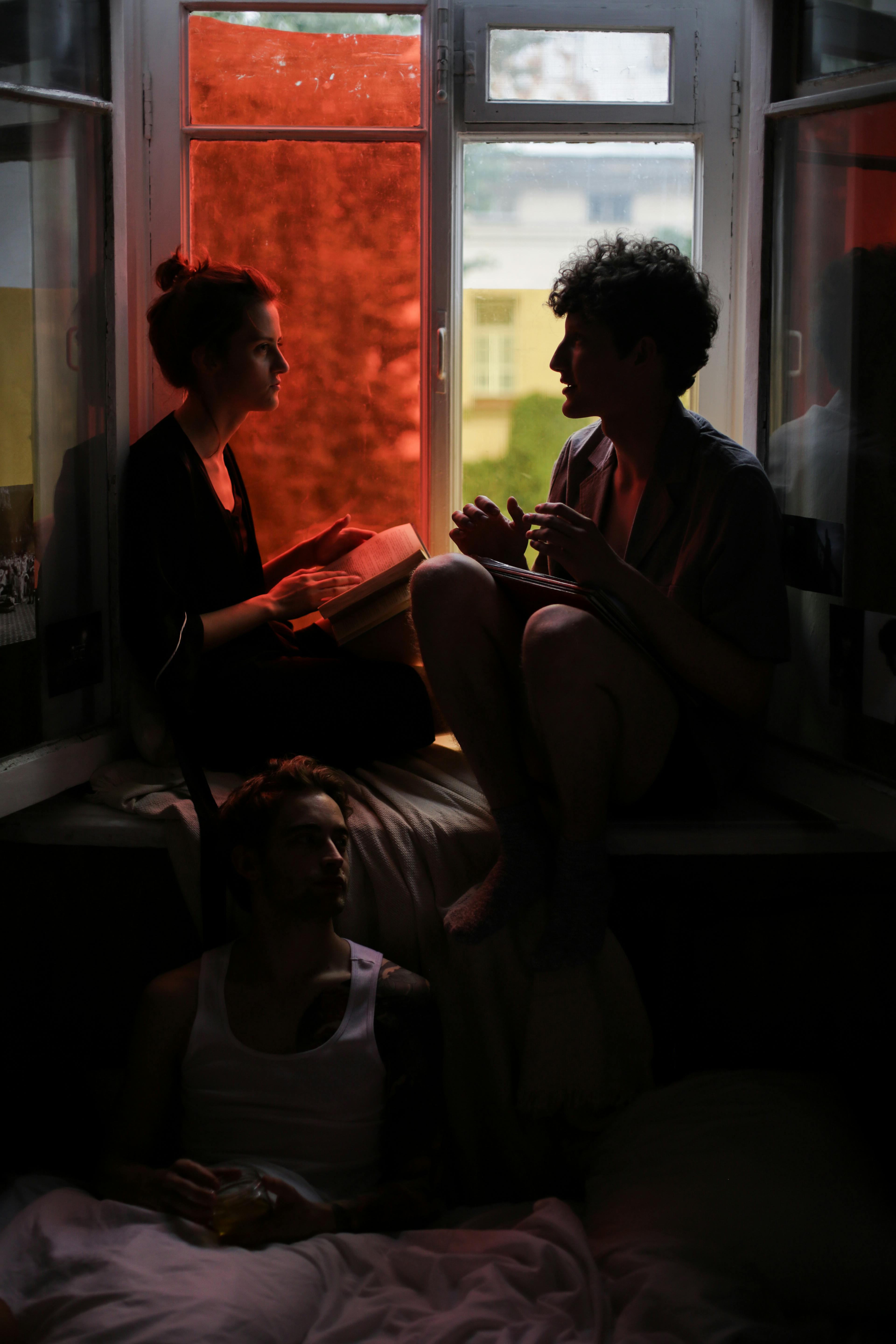 woman sitting on window talking to a man while husband is sitting alone